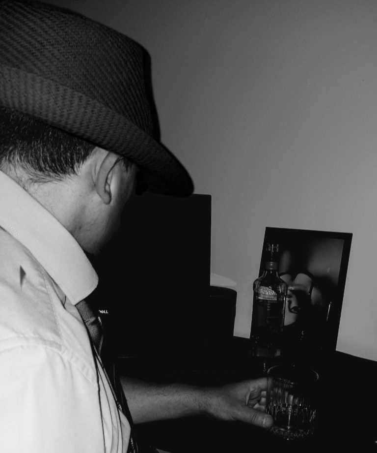 John Raven looking longingly at photo of beautiful woman and drinking whisky.